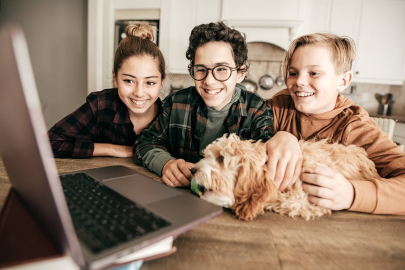 Teens in domestic kitchen watching a video on a computer.