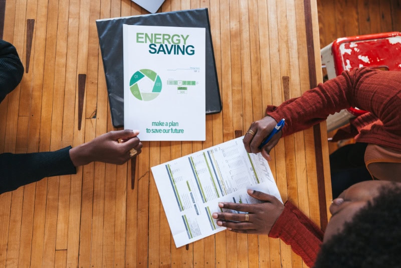 2025 Heat Pump Buying Guide for Michigan Homes. A young woman financial advisor is helping a customer to sign a new contract about energy saving and green sustainable resources.